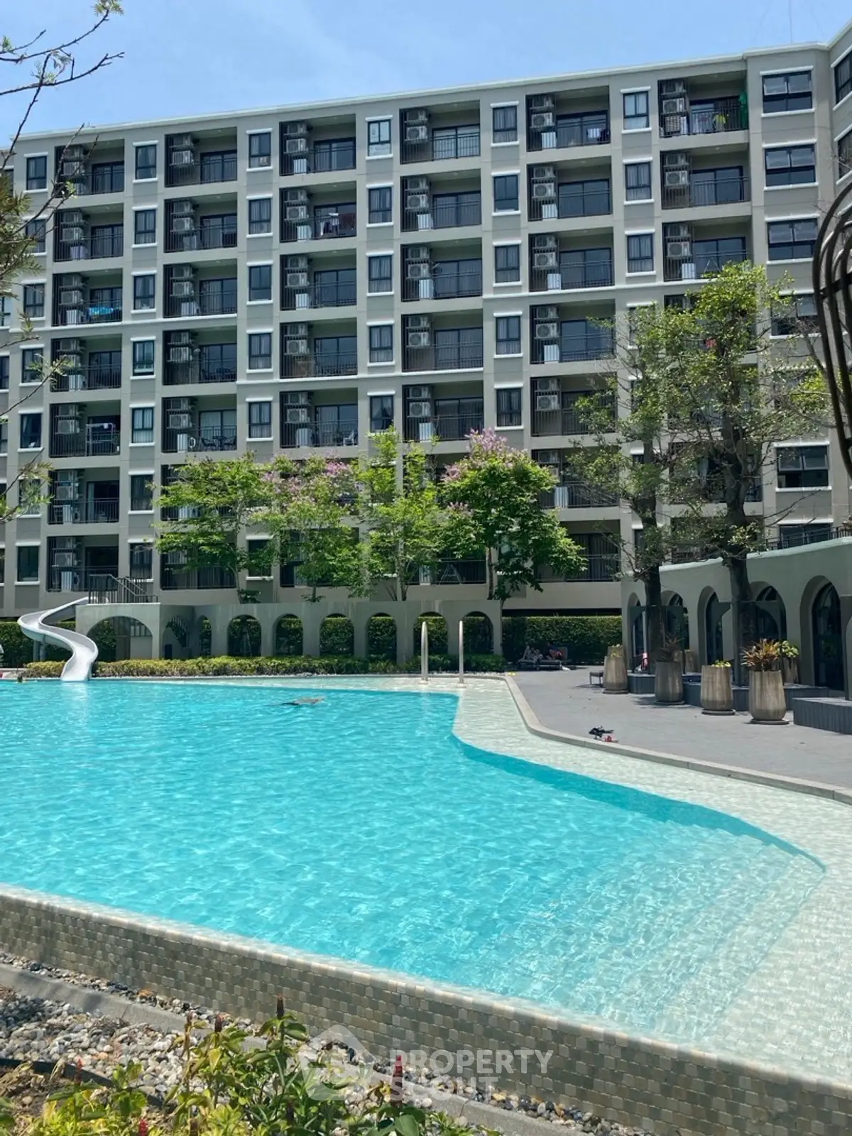 Modern apartment building with a large swimming pool and lush greenery, perfect for relaxation and leisure.
