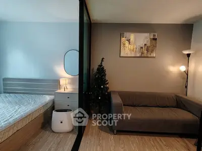 Modern studio apartment with cozy living area and stylish bedroom separated by glass partition.
