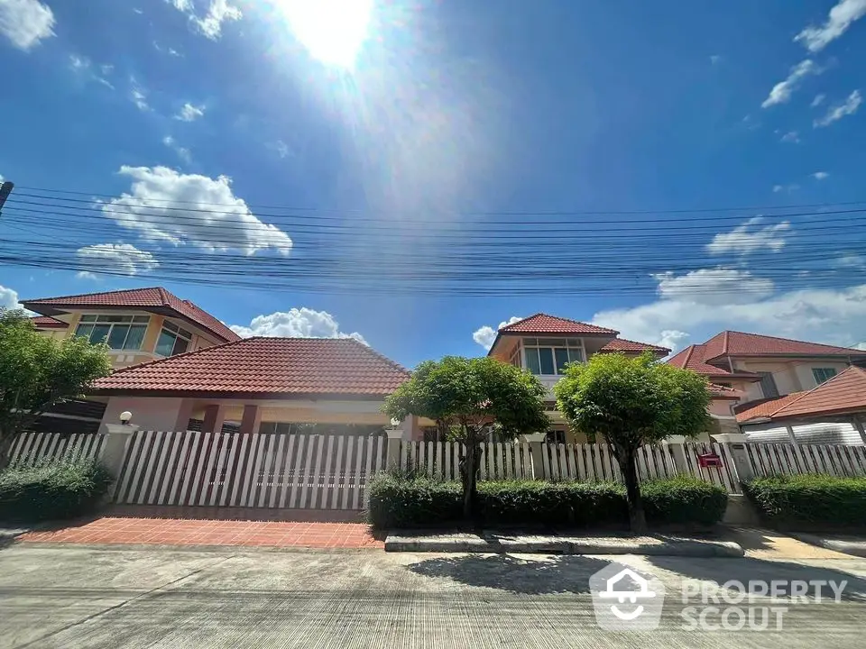 Charming suburban house with red roof and lush greenery under a clear blue sky.