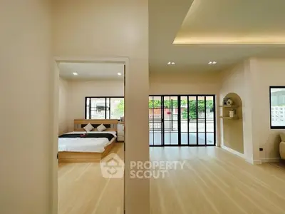 Spacious modern bedroom with large windows and open living area, featuring sleek wooden flooring.