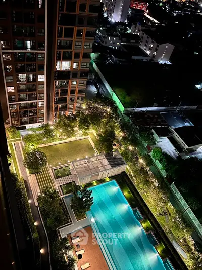 Stunning aerial view of luxury condominium with illuminated pool and lush garden at night.