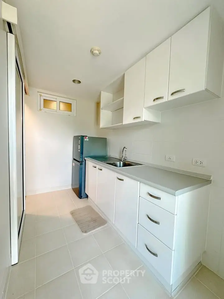 Modern kitchen with sleek white cabinets and compact fridge in a bright, minimalist design.