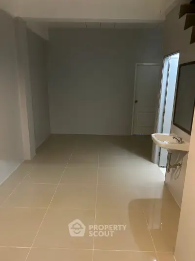 Spacious empty room with tiled flooring and a wall-mounted sink, ideal for customization.