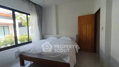 Bright and airy bedroom with large window and wooden door, offering a serene and inviting atmosphere.