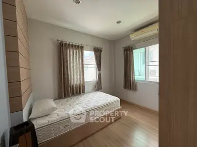 Cozy bedroom with wooden flooring and ample natural light, featuring a single bed and air conditioning.