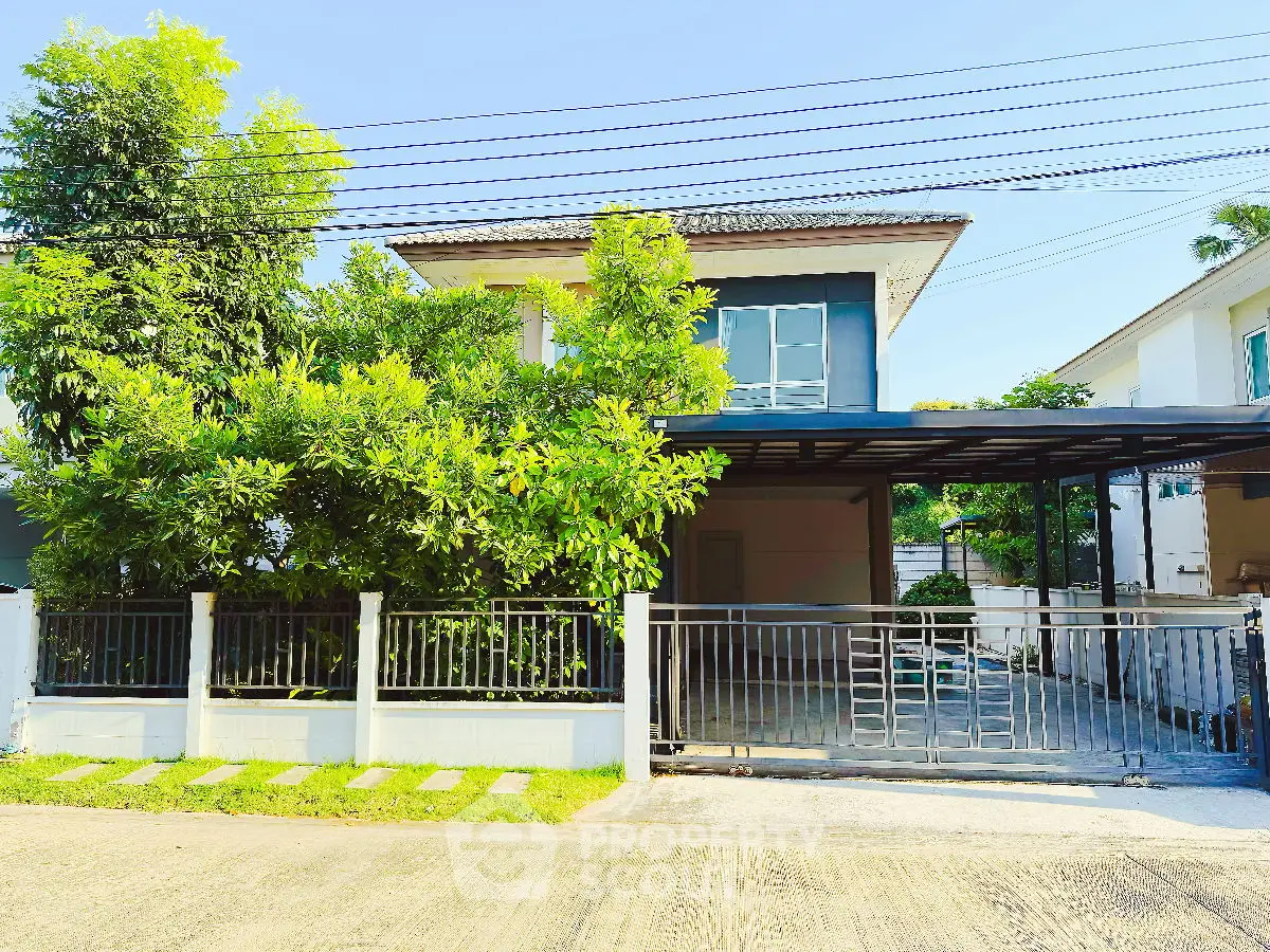Charming two-story house with lush greenery and gated driveway in a serene neighborhood.