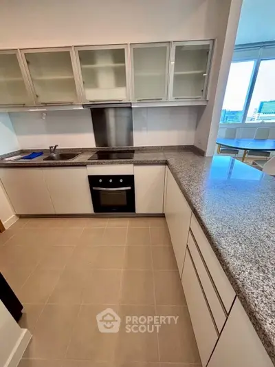 Modern kitchen with sleek countertops and built-in oven, featuring ample cabinet space and natural light.