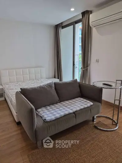 Modern studio apartment with cozy sofa and bed, featuring air conditioning and natural light.