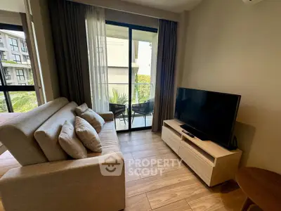 Modern living room with cozy sofa and TV, opening to a balcony with outdoor seating.
