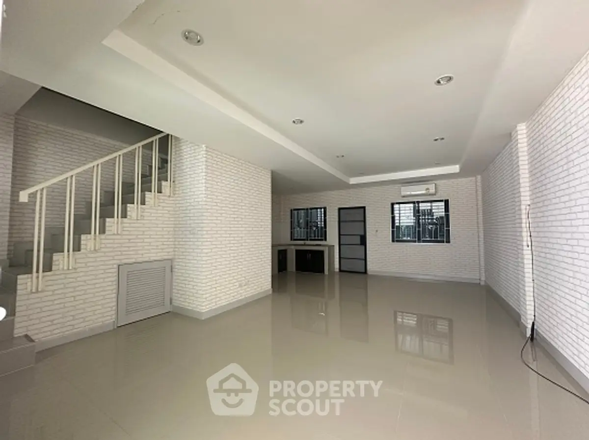 Spacious modern living room with sleek staircase and large windows in a contemporary home.