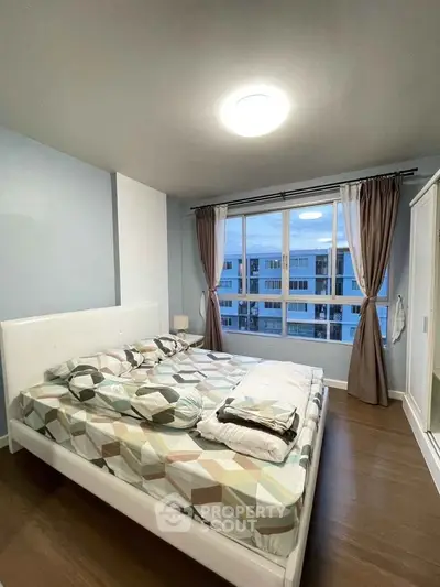 Cozy bedroom with large window offering city view, featuring modern decor and ample natural light.
