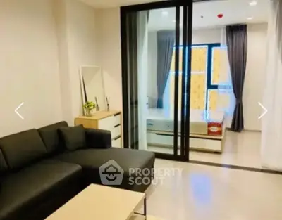 Modern living room with sleek black sofa and glass partition leading to a bright bedroom.