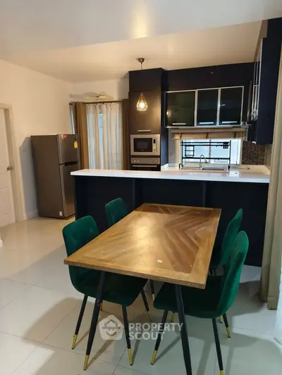 Modern kitchen with sleek black cabinets, wooden dining table, and green chairs in a stylish apartment.