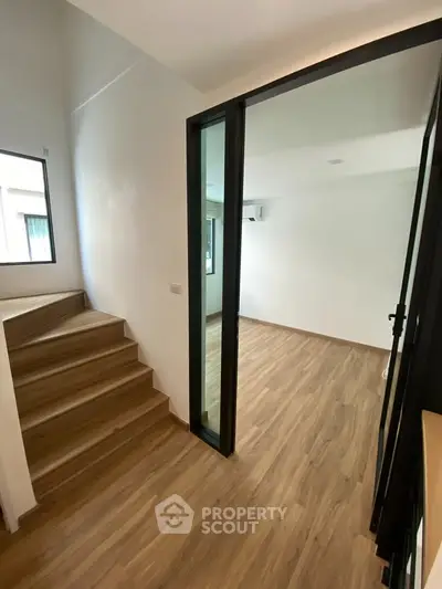 Modern interior with wooden flooring and sliding glass door, leading to a bright room.