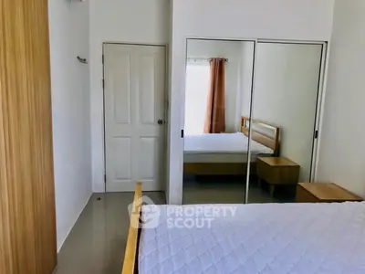 Modern bedroom with mirrored closet and wooden furniture, bright and inviting space.