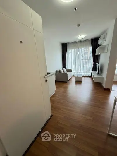 Modern living room with wooden flooring and large window, featuring a cozy sofa and wall-mounted TV.