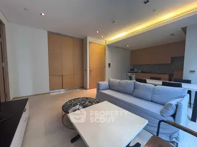 Modern living room with open kitchen, featuring sleek furniture and ambient lighting.