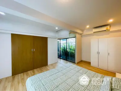 Spacious bedroom with wooden flooring and large closet, featuring a balcony with greenery.