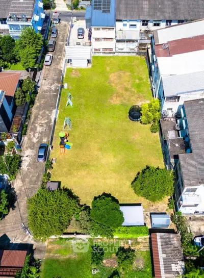 Aerial view of spacious urban garden with playground and trampoline, surrounded by residential buildings.