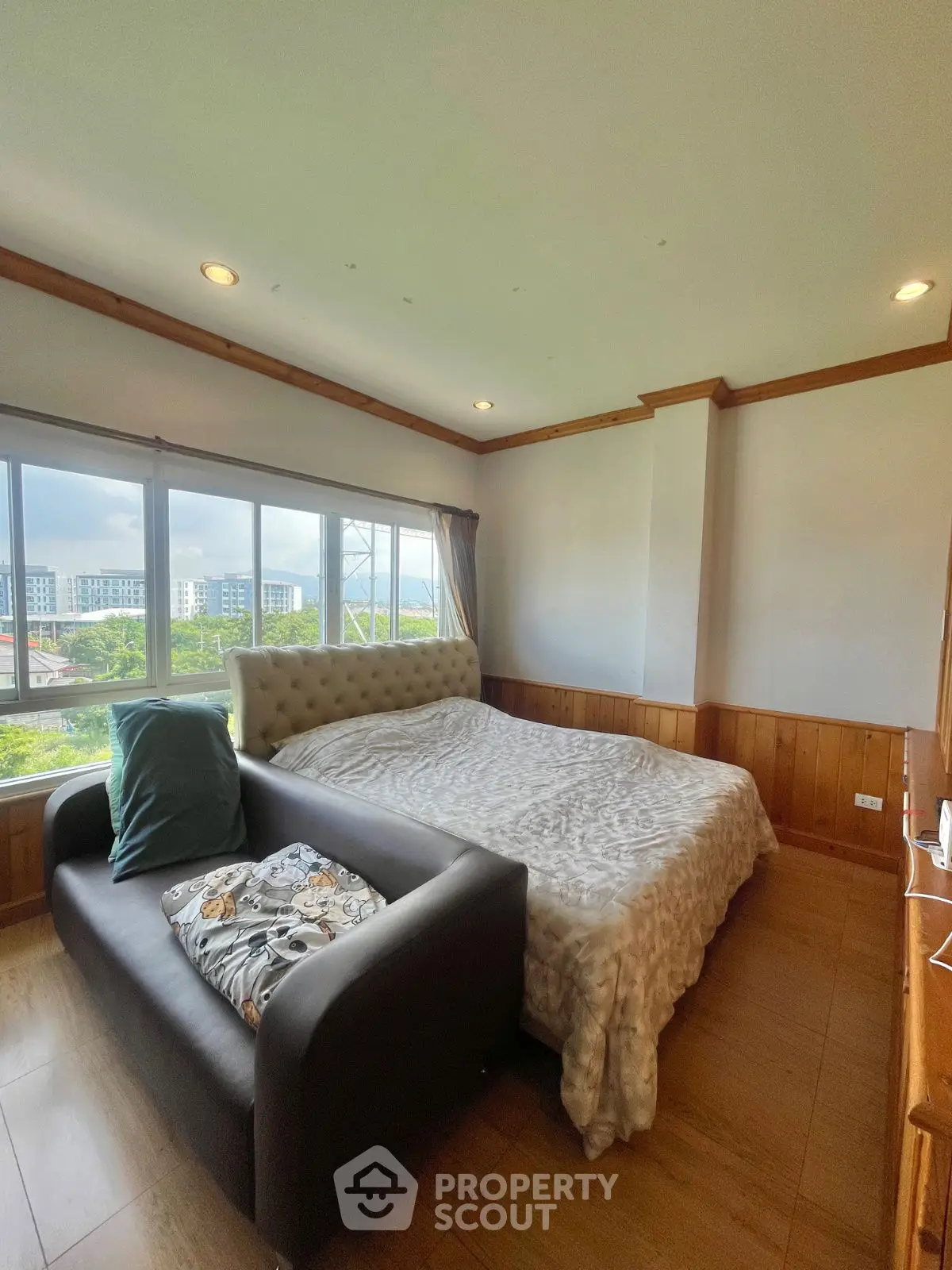 Cozy bedroom with large windows offering a scenic view, featuring a plush bed and stylish sofa.