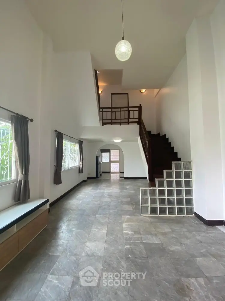 Spacious two-story home interior with high ceilings, natural light, and a grand staircase leading to an inviting mezzanine level.