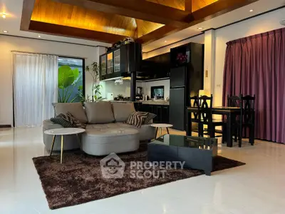 Spacious living room with modern decor and open kitchen layout, featuring elegant wooden ceiling and cozy seating area.