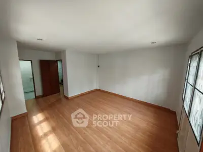 Spacious empty room with wooden flooring and ample natural light.