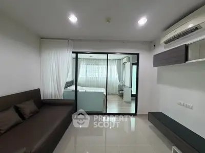 Modern living room with sleek design and glass partition leading to bedroom, featuring air conditioning and stylish decor.
