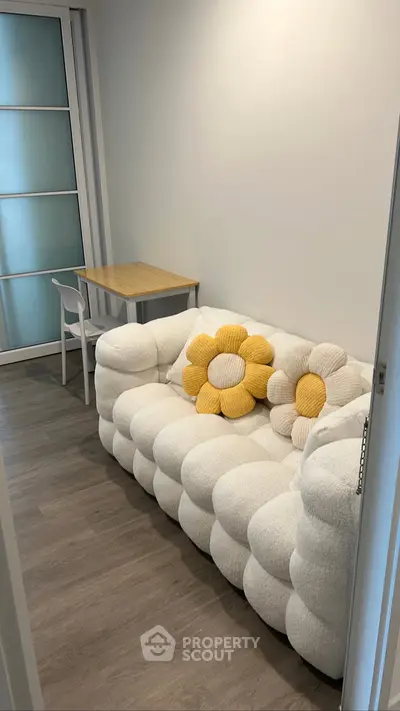 Cozy living room with plush white sofa and floral cushions, adjacent to a small dining table.