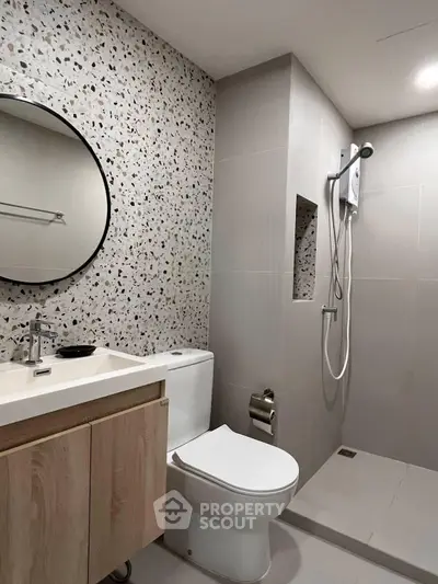 Modern bathroom with terrazzo wall, round mirror, and sleek fixtures.
