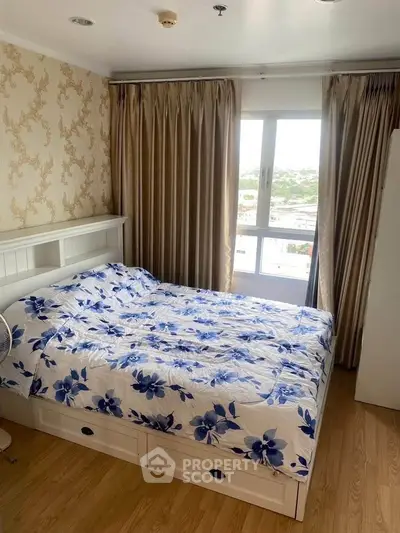 Cozy bedroom with floral bedding and large window offering natural light and city view.