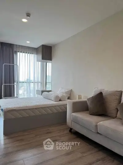 Modern bedroom with cozy sofa and large window offering natural light and city view.