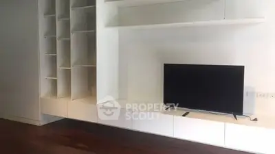 Modern living room with sleek built-in shelving and flat-screen TV on wooden floor.