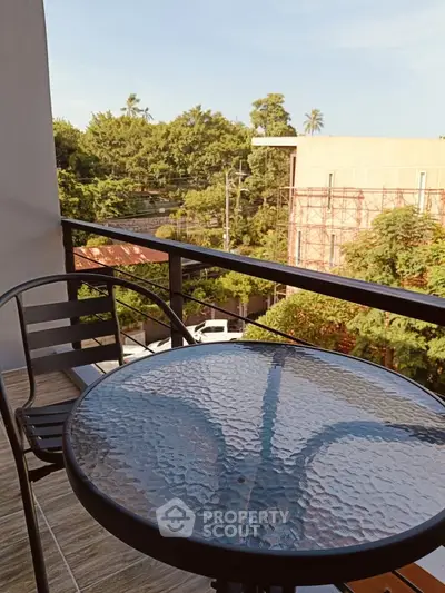 Charming balcony with glass table and lush green view, perfect for relaxation.