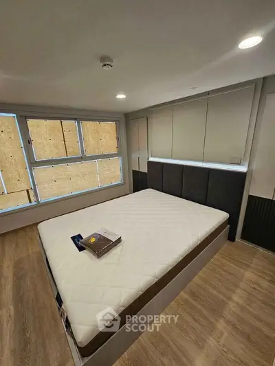 Modern bedroom with large window and stylish decor, featuring a comfortable bed and wooden flooring.