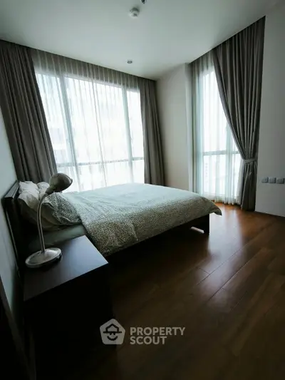 Cozy bedroom with large windows and elegant curtains, featuring a modern bed and sleek wooden flooring.