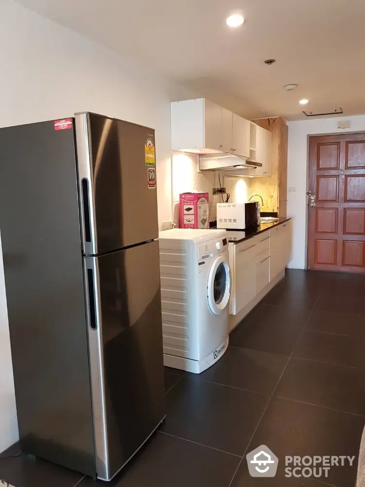 Modern kitchen with sleek appliances including fridge and washing machine in stylish apartment.