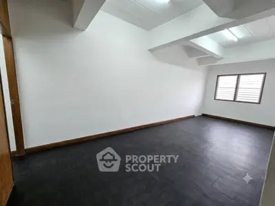 Spacious empty room with dark flooring and bright natural light from window.