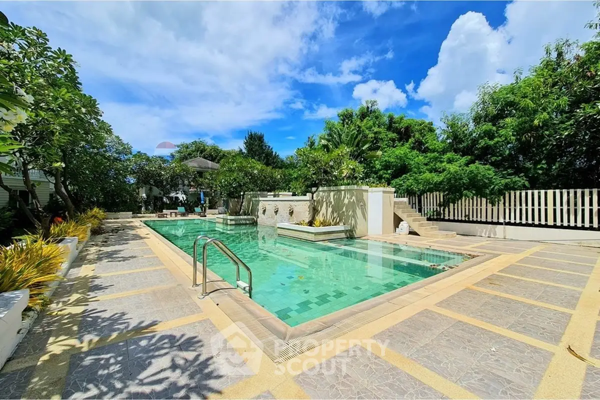 Luxurious outdoor pool area with lush greenery and clear blue sky, perfect for relaxation and leisure.