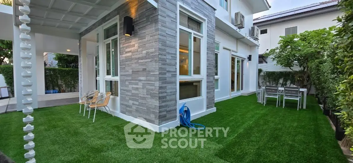 Modern house exterior with lush green lawn and outdoor seating area.