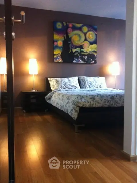 Cozy bedroom with wooden flooring and stylish decor, featuring a modern bed and artistic wall painting.