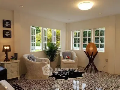 Charming living room with wicker chairs and large windows overlooking lush greenery.