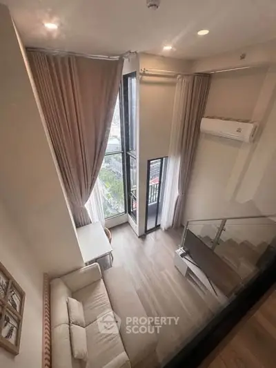 Modern loft-style living room with high ceilings and large windows offering a stunning city view.