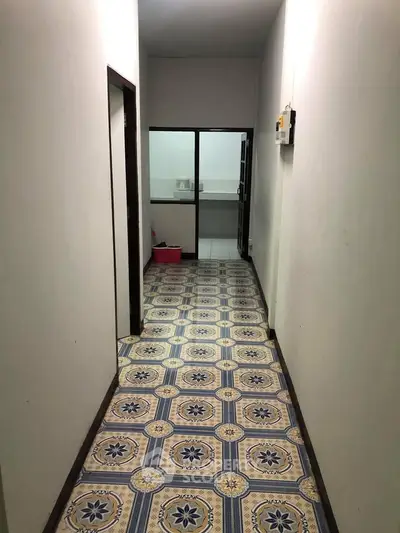 Narrow hallway with patterned tile flooring leading to a small kitchen area.