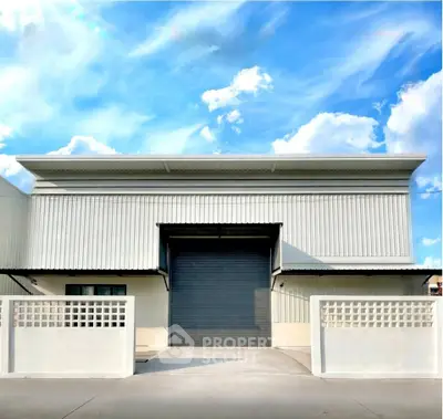 Modern industrial warehouse with sleek design and spacious entrance under a clear blue sky.