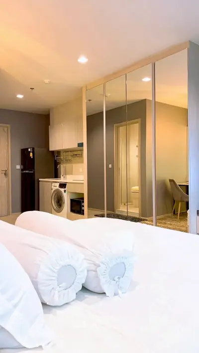 Modern bedroom with mirrored closet and compact kitchen featuring washing machine and fridge.