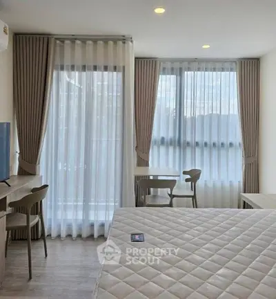 Modern bedroom with large windows and elegant curtains, featuring a cozy seating area and stylish decor.