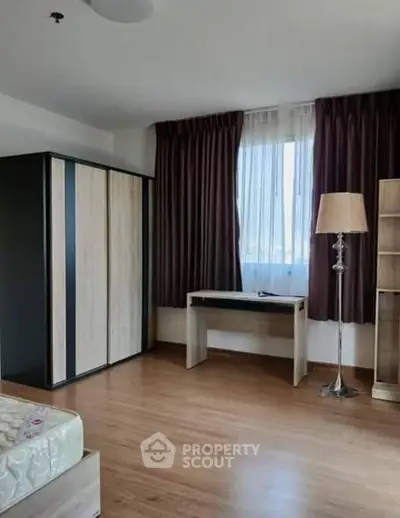 Spacious bedroom with wooden flooring, large wardrobe, and natural light from window.