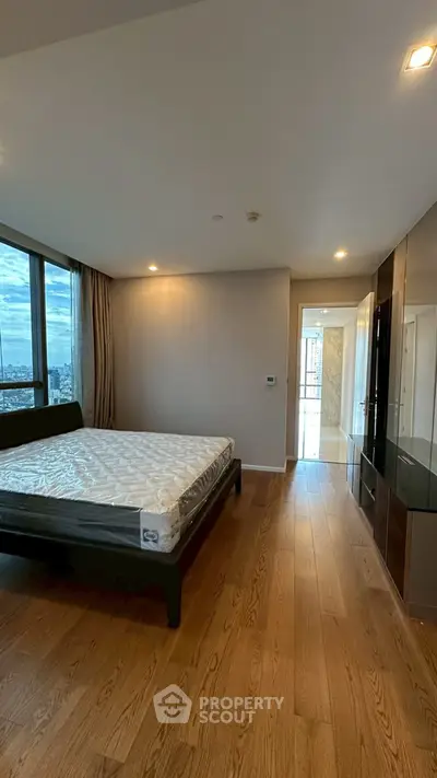 Spacious bedroom with large windows and wooden flooring in modern apartment