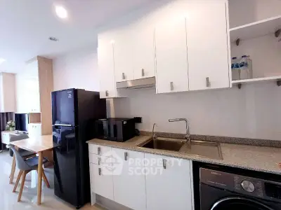Modern kitchen with sleek white cabinets, granite countertops, and appliances including fridge and washing machine.
